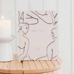 a book sitting on top of a wooden table next to a white vase and candle