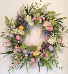 an easter wreath with flowers and eggs on the front is hung on a white wall