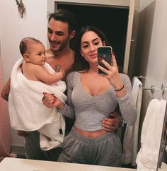 a man and woman taking a selfie in front of a bathroom mirror holding a baby