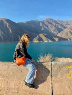 a woman sitting on top of a stone wall next to a large body of water