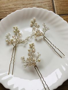 three hair pins with pearls on them are sitting on a white plate, resting on a wooden table