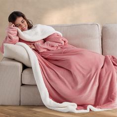 a woman laying on a couch wrapped in a pink blanket and covering her face with a white sherpam