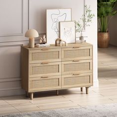 a room with a dresser, lamp and pictures on the wall next to potted plants