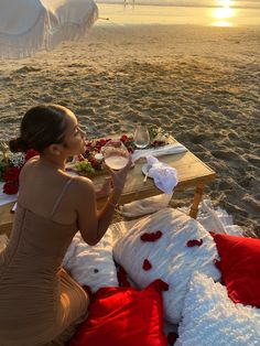 a woman sitting at a table on the beach with food and drinks in front of her