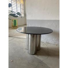 a round table sitting on top of a cement floor next to a window with shutters