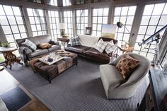 a living room filled with lots of furniture next to large windows and floor to ceiling windows