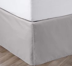 a bed with a white sheet on top of it and wood flooring in the background