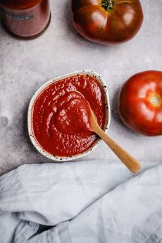 a wooden spoon sitting in a bowl filled with ketchup next to two tomatoes