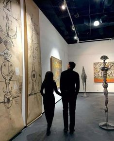 two people are looking at artwork on display in an art gallery, one is holding the hand of another person's hand