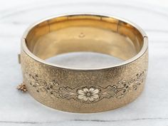 "This vintage, hinged, floral black enamel bracelet is in exquisite condition, with a beautiful, high polish to the gold-filled metal. The engraving on the top is intricate, and detailed with flowers, and swirls creating a lovely texture on the wrist. The inside center is plain, allowing for an engraving of your very own! Metal: Gold Fill Material: Black Enamel Width: 25.5 mm Inside circumference: 7 Inches Marks: \"1/20 12K T.G.R.\" Stamped on the inside band To view a video of this piece check out the link below: https://vimeo.com/822132737 SKU #: A25529 Each piece has been identified and graded by a Graduate Gemologist who has been certified by the Gemological Institute of America (GIA). We have six brick-and-mortar storefronts in Maine, Massachusetts and New Hampshire and have been in b Bracelet Stacking, Victorian Revival, Aquamarine Pendant, Filigree Pendant, Antique Brooches, Floral Pendant, Wedding Jewelry Bracelets, Rose Gold Band, Enamel Bracelet