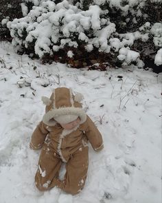 a baby sitting in the snow wearing a brown outfit