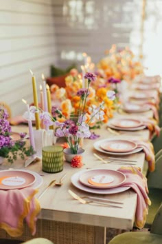 the table is set with pink and yellow plates, napkins, candles and flowers