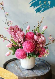 a white vase filled with pink flowers on top of a wooden table