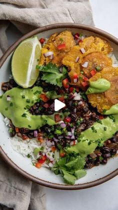 a white plate topped with rice, black beans and guacamole next to a lime wedge