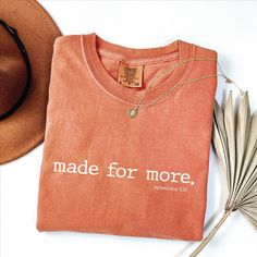 a t - shirt that says made for more on it next to a hat and feather