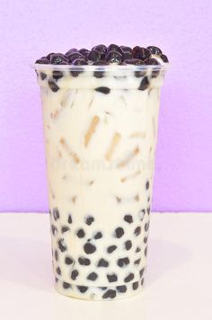 a cup filled with milk and blueberries on top of a white table next to a purple wall