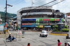 people walking and riding bikes on the street in front of a large building with many shops