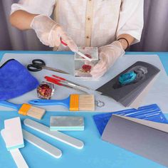 a woman in white shirt and gloves with various items on blue table top next to scissors