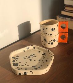 two ceramic dishes sitting on top of a wooden table next to books and a cup