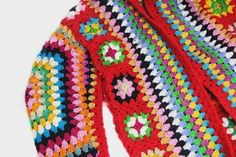 a colorful crocheted sweater is laying on the floor with it's hood up