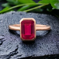 a close up of a ring with a red stone in the middle on a rock