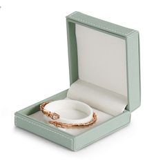 an open green box with a ring and bracelet in it on a white table top