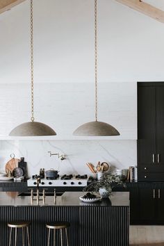 an open kitchen with black cabinets and pendant lights hanging from the ceiling over the island