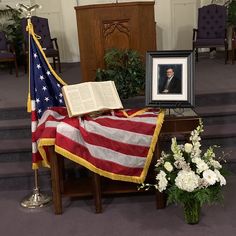 an american flag draped in front of a book on a table with flowers next to it