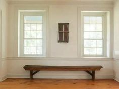 an empty room with two windows and a wooden bench