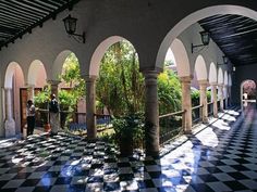 an outdoor area with black and white checkered tile flooring, arches and trees