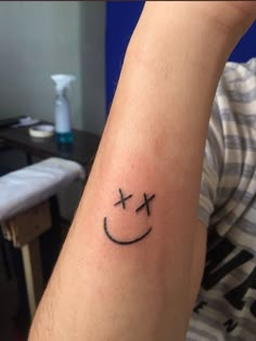 a person with a smiley face tattoo on their arm and the cross is in the middle