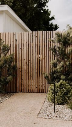 a wooden fence next to a white house and some bushes in front of the building