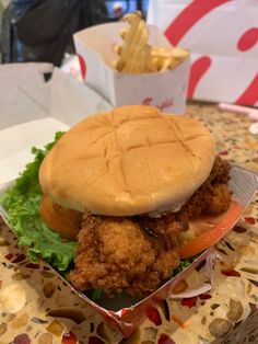 a chicken sandwich with lettuce, tomato and fries in a box on a table