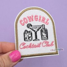 someone holding up a small patch with the words cowgirl cocktail club on it and two glasses