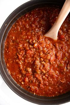 a wooden spoon in a pot filled with chili and ground beef sauce on top of a white table