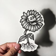 a person holding up a sticker with a flower on it's face and roots