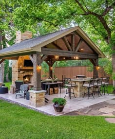 a covered patio with an outdoor kitchen and grill in the back yard, surrounded by trees