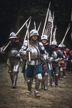 a group of people dressed in medieval armor and holding flags walking down a grass covered field