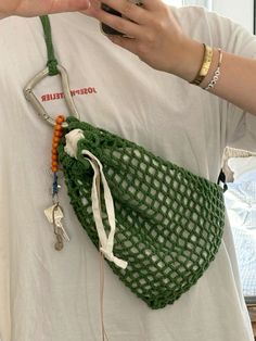 a woman holding a cell phone in her hand and wearing a green netted bag