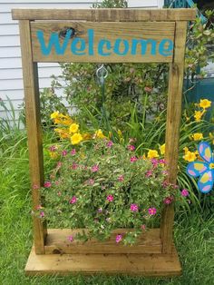 a wooden welcome sign sitting in the grass next to flowers and a butterfly on it