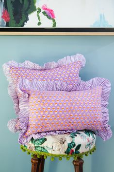 three pillows sitting on top of a stool in front of a wall with a painting