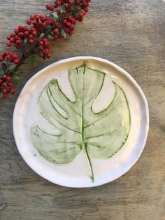 a white plate with a green leaf on it next to red berries and greenery