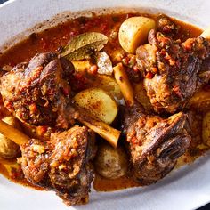 a white plate topped with meat and potatoes on top of a blue table cloth covered in sauce