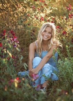 a woman sitting in the middle of a field full of flowers smiling at the camera