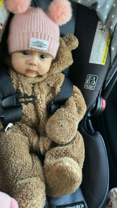 a baby in a car seat wearing a teddy bear hat