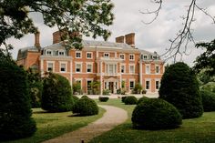 a large red brick building surrounded by trees and bushes in front of it is a pathway leading to the entrance