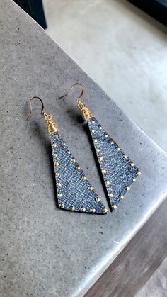 the denim triangle earrings with gold studding are on top of a marble countertop