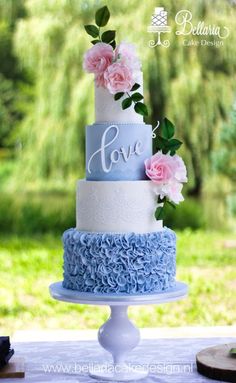 a blue and white wedding cake with pink flowers on the top is sitting on a table