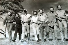 an old black and white photo of men in uniforms posing for a group shot with trees in the background