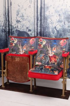 two red chairs sitting next to each other in front of a wall with pictures on it